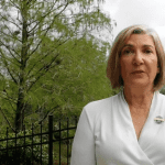Woman in white blouse giving a speech outside.