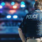 Police Officer standing in front of squad car with lights on